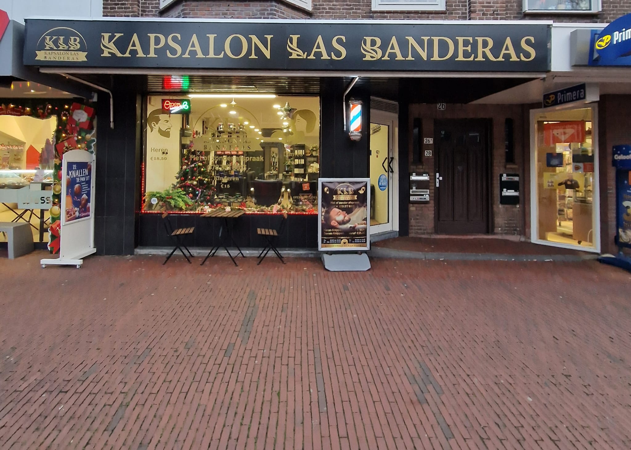 De ingang van Kapsalon Las Banderas met het zwart-gouden gevelbord aan de Damlaan